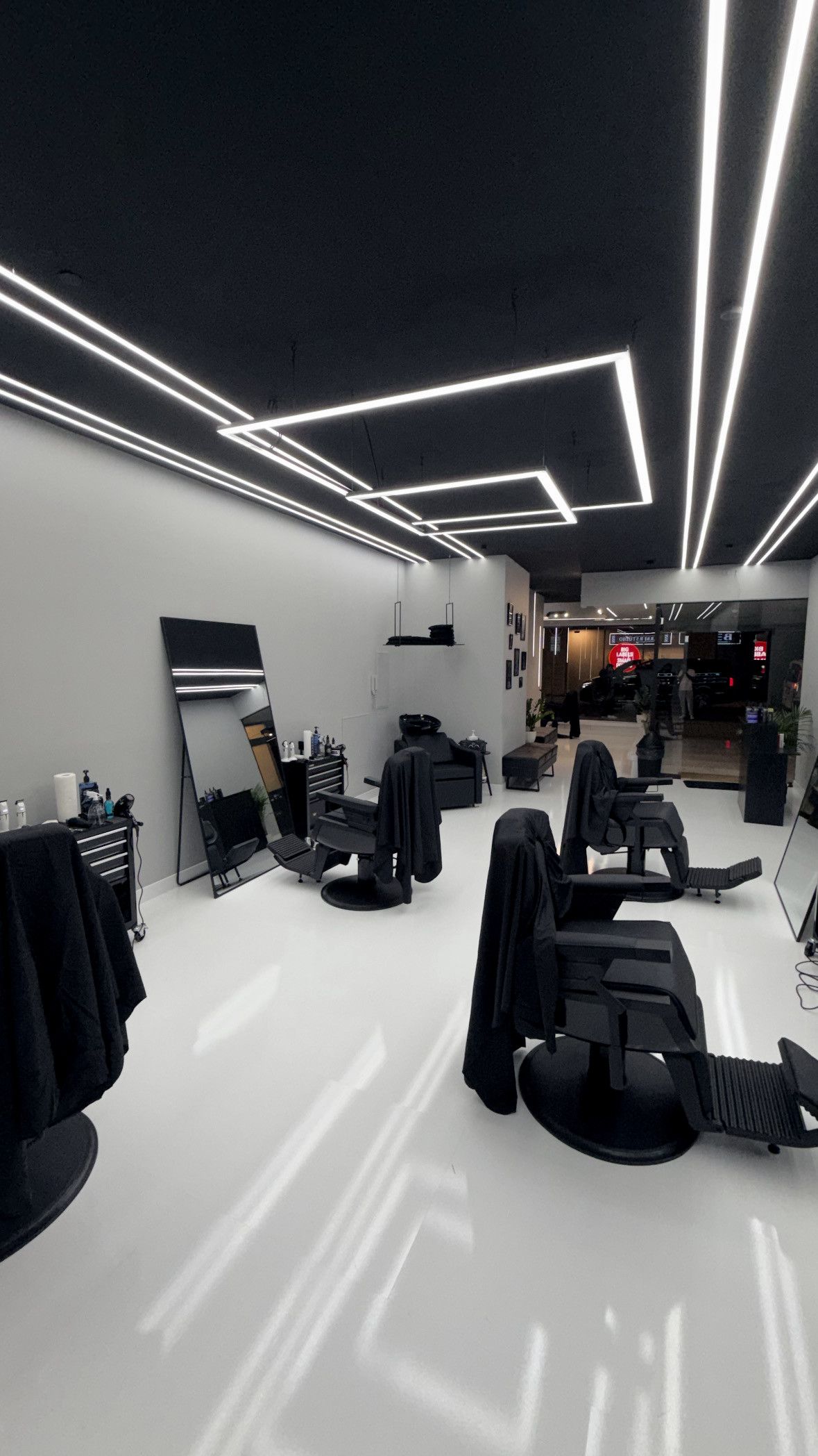 Blick durch das Studio: schwarze Decke mit LED-Linien, weißer Boden, Barberstühle vor großen Spiegeln
